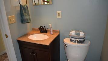 Une salle de bain avec un lavabo blanc, un meuble en bois foncé et des toilettes, à côté desquelles se trouve un panier rempli de serviettes pliées.