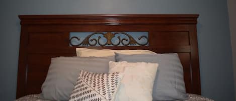 Una camera da letto con testiera in legno, un letto con biancheria a motivi decorativi e un cartello appeso al muro con la scritta 'LOVE' e la sagoma di un uccello.