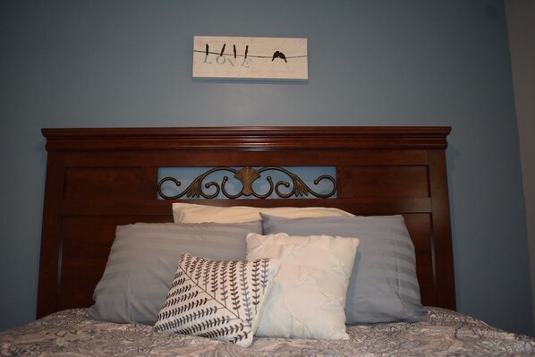 Un dormitorio con cabecera de madera, cama con ropa de cama estampada y un cartel en la pared con la palabra 'LOVE' y la silueta de un pájaro.