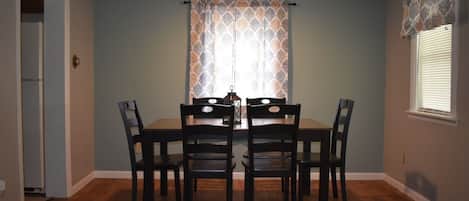 A dining area with a table and four chairs, a ceiling light, and patterned curtains.