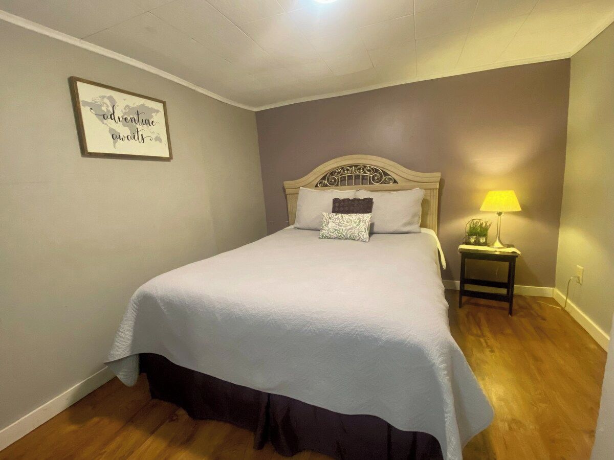 A bedroom with a bed, a nightstand with a lamp, and a wall-mounted picture.