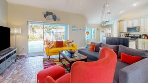 Ein modernes Wohnzimmer mit einem gelben Sofa, einem grauen Sofa und roten Sesseln. Es gibt eine Küchenzeile mit weißen Schränken und einer Mikrowelle.