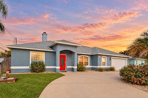 A residential house with a red door, a garage, and a well-maintained lawn.