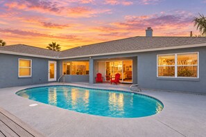 A residential property with a swimming pool, a deck, and a patio area with red chairs.