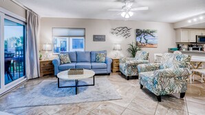 A living room with a blue sofa, patterned armchairs, a coffee table, and a ceiling fan. - Dreamy oasis on the beach with balcony, pools, gym & ocean view - dog-friendly (St. Augustine)