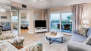 A spacious living room with a flat-screen TV, a sofa, a coffee table, and a balcony with a view. - Dreamy oasis on the beach with balcony, pools, gym & ocean view - dog-friendly (St. Augustine)