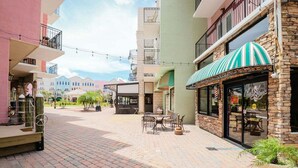 Um pátio com mesas ao ar livre, um restaurante com toldo listrado e edifícios com varandas.