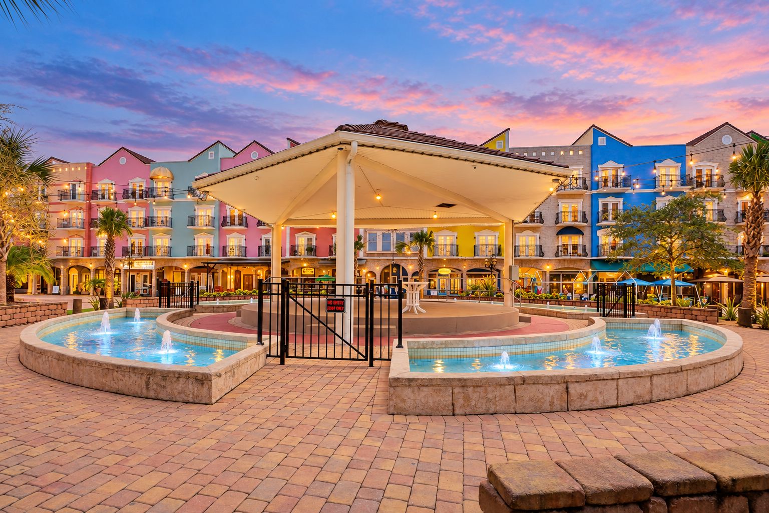 A hotel courtyard with a central fountain, a covered seating area, and colorful buildings in the background.
