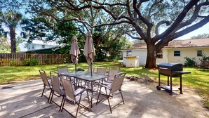 A patio with a metal table and chairs, a barbecue grill, and a large tree providing shade. - Spacious Pet -Friendly Home w/ Fenced in Yard and Close to The Beach (St. Augustine)