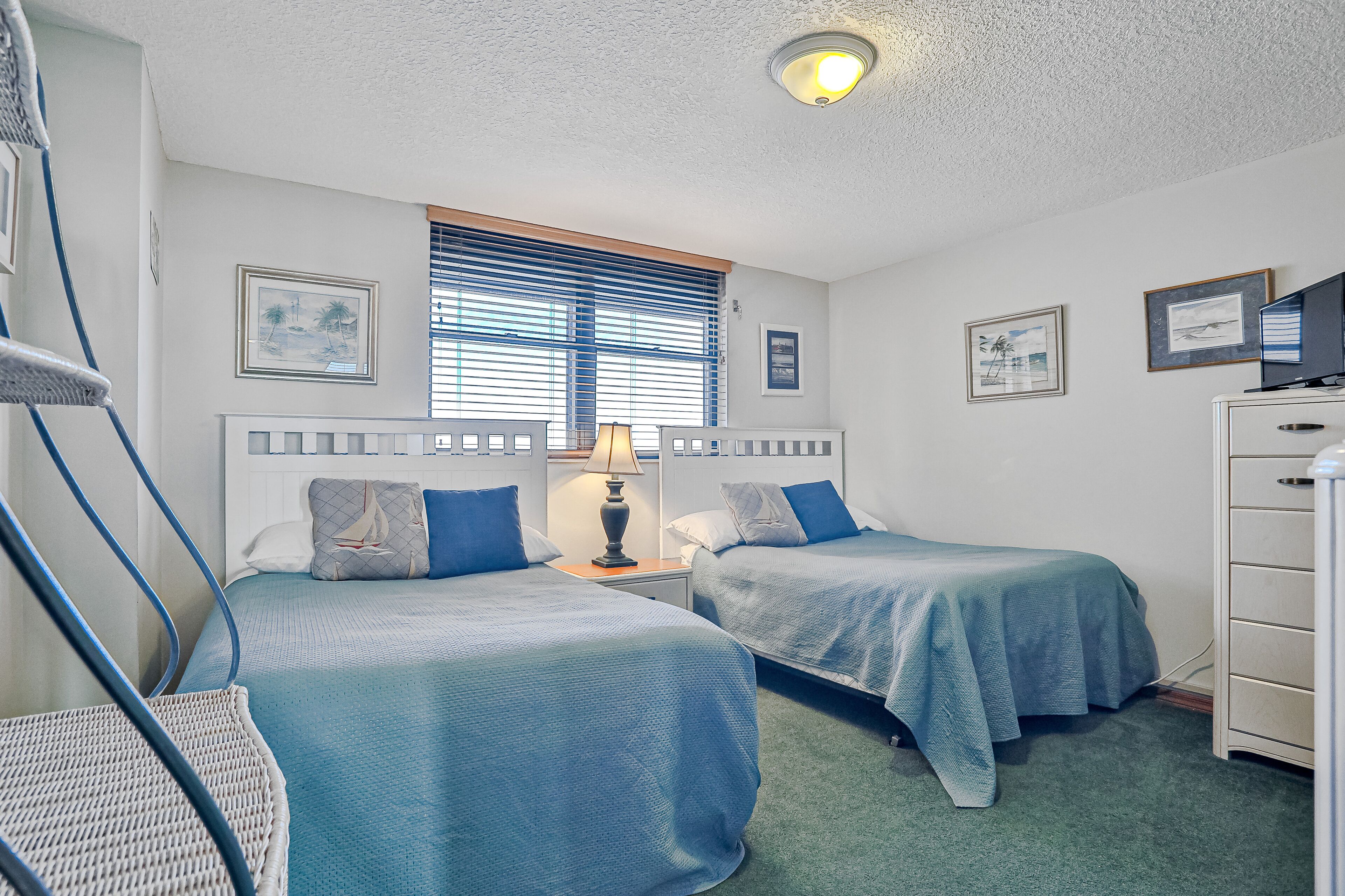 A hotel room with two beds, a desk, a chair, and a dresser.
