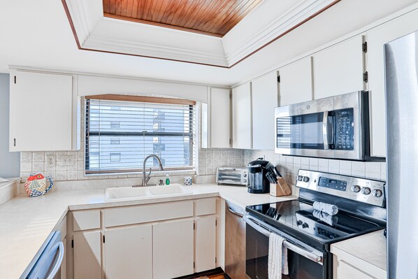 A modern kitchen with white cabinets, a stainless steel microwave, a stove, and a sink.