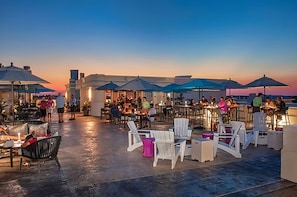 An outdoor seating area with tables and chairs, umbrellas, and a view of the sunset. - Home 1 Block from 2 Beaches w/Private Pool, High-Speed WiFi & Central AC (St. Augustine)
