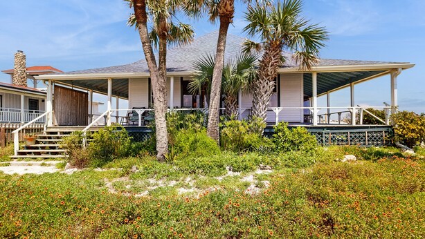 A coastal house with a covered porch, palm trees, and a sandy garden. - Fabulous oceanfront home with ocean view, WiFi, washer/dryer, & central AC (St. Augustine)