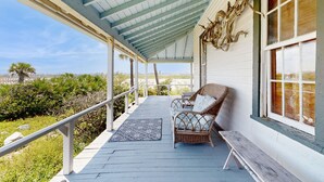 A covered porch with wicker furniture and a bench, overlooking a coastal landscape. - Fabulous oceanfront home with ocean view, WiFi, washer/dryer, & central AC (St. Augustine)