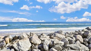 A rocky shoreline with waves crashing onto the beach under a clear blue sky. - Fabulous oceanfront home with ocean view, WiFi, washer/dryer, & central AC (St. Augustine)