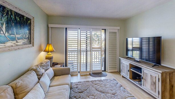 A living room with a sofa, a TV, a lamp, and a sliding glass door leading to a balcony.