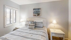 A bedroom with a bed, two nightstands, a ceiling fan, a window with shutters, and a painting on the wall.