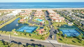 An aerial view of a coastal resort with multiple buildings, a marina, and tennis courts.