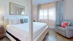 A bedroom with a large bed, a bedside table, a chair, a window with curtains, and a ceiling fan. - A1A South St Augustine | 2 bedroom Oceanview Condo | Sleeps 8 (St. Augustine)