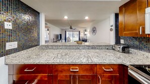 Une cuisine moderne dotée d’un plan de travail en granit, de meubles en bois et d’un pare-feu orné de carreaux de mosaïque bleus.