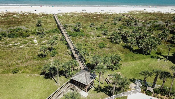 Vue aérienne d’une plage avec une promenade en bois menant à un bâtiment doté d’un toit en pente.