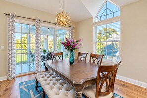 A dining room with a wooden table, six chairs, a vase with flowers, and a chandelier.