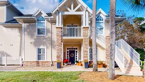 A two-story house with a balcony, a front porch with potted plants, and a staircase leading to the second floor. - Spacious condo with pool, hot tub and private washer/dryer (St. Augustine)