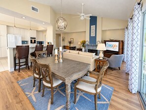 A spacious living area with a dining table, chairs, a sofa, and a television displaying a logo.