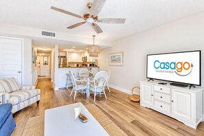 A modern living room with a television, white furniture, and a dining area.