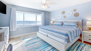 A bedroom with a bed, a desk, a chair, a ceiling fan, a window with curtains, and wall clocks. - Oceanfront rental with amazing views, beach access, pools, tennis & pickleball (St. Augustine)