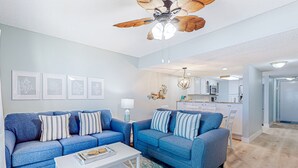 A modern living room with two blue sofas, a white coffee table, and a ceiling fan. - Oceanfront rental with amazing views, beach access, pools, tennis & pickleball (St. Augustine)
