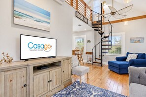 A modern living room with a flat-screen TV, a staircase, and a blue sofa.
