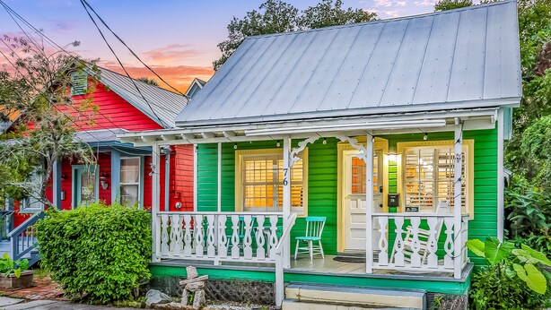 Une maison à deux étages avec un porche, un revêtement extérieur vert et un toit rouge.