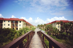 A wooden bridge leading to a hotel with red roofs and multiple balconies, surrounded by greenery and palm trees. - Lovely Oceanside Home w/Outdoor Shower/Free WiFi/Shared Pool/Hot Tub/Tennis/AC (St. Augustine)