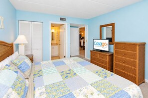 A bedroom with a large bed, a dresser, a television, and a door leading to a bathroom. - Lovely Oceanside Home w/Outdoor Shower/Free WiFi/Shared Pool/Hot Tub/Tennis/AC (St. Augustine)