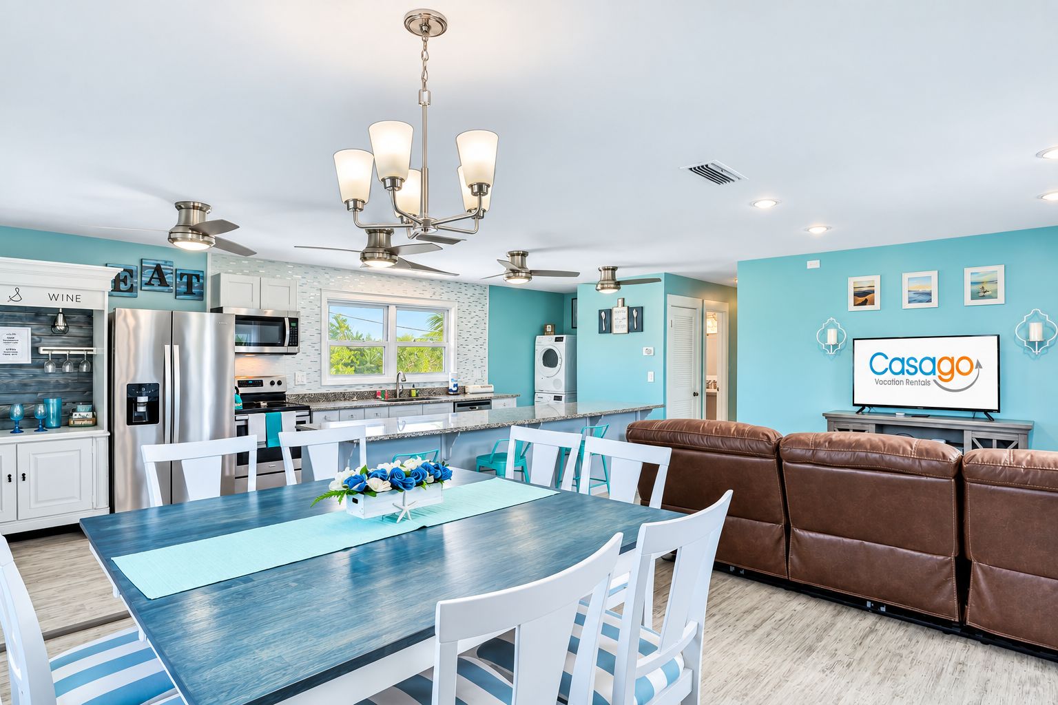 A modern kitchen with stainless steel appliances, a dining area with a blue table, and a living area with a brown sofa.