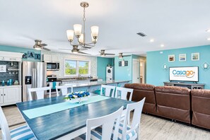 Une cuisine moderne équipée d’appareils électroménagers en acier inoxydable, un coin repas avec une table bleue et un salon avec un canapé marron.