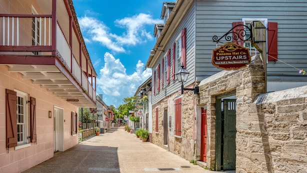 Une rue étroite bordée de bâtiments historiques, dont un où se trouve une entreprise spécialisée dans la vente de chapeaux de Panama, dont l’enseigne est visible à l’étage.