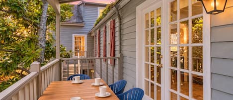 A wooden deck with a table and chairs, a covered area with a railing, and a building with large windows and a door.