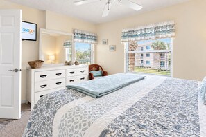 A bedroom with a bed, dresser, chair, and windows with curtains. - Freedom By The Sea II with ocean views, 2 pools, tennis & gym - steps to beach (St. Augustine)