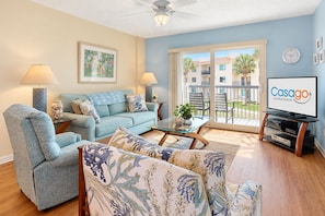 A living room with a sofa, armchair, coffee table, and a flat-screen TV. - Freedom By The Sea II with ocean views, 2 pools, tennis & gym - steps to beach (St. Augustine)