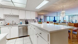 Een moderne keuken met witte kasten, een inbouwvaatwasser en een groot eiland met zitplaatsen.