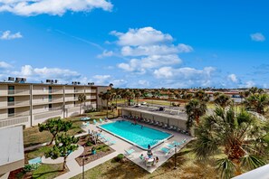 A hotel with a swimming pool, outdoor seating, and palm trees.