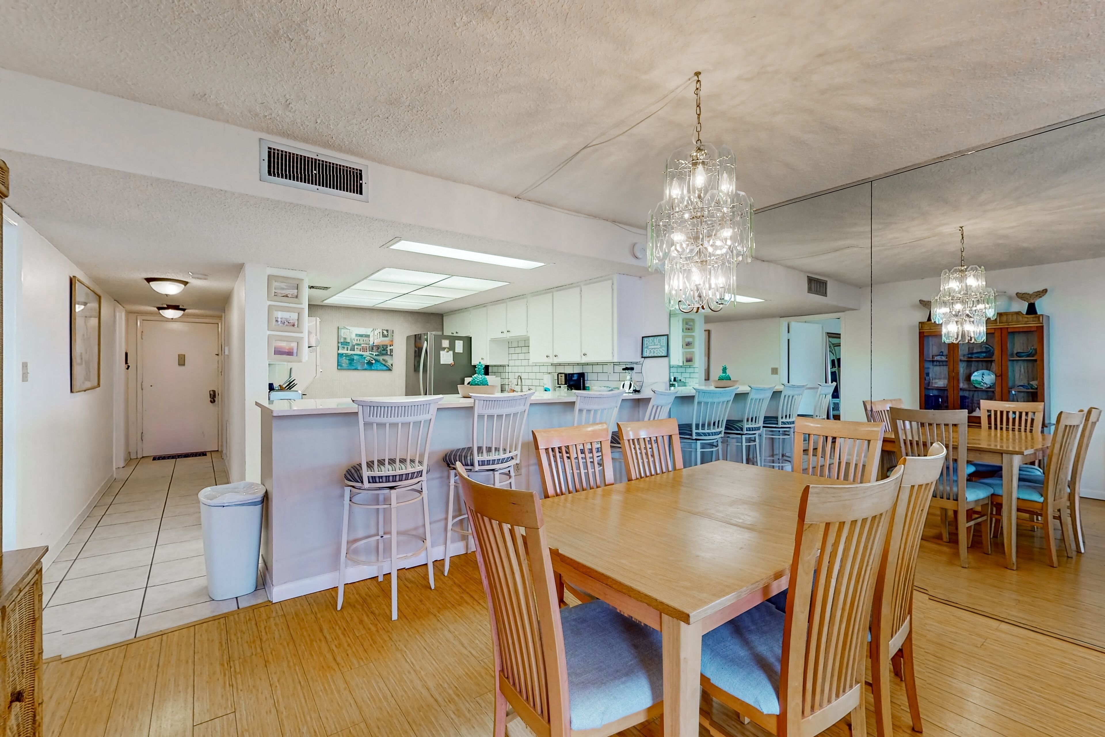 Une cuisine spacieuse avec des meubles blancs, un îlot central et un coin repas agrémenté de tables et de chaises en bois.