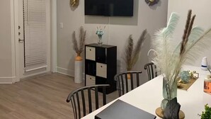 Una sala de estar moderna con un televisor de pantalla plana, una mesa de comedor, sillas y objetos decorativos.
