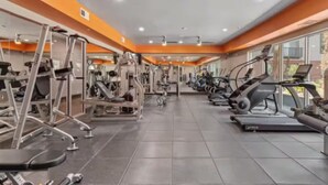 Un gimnasio con diversos equipos de ejercicio, como cintas de correr y máquinas de pesas, organizados en filas.