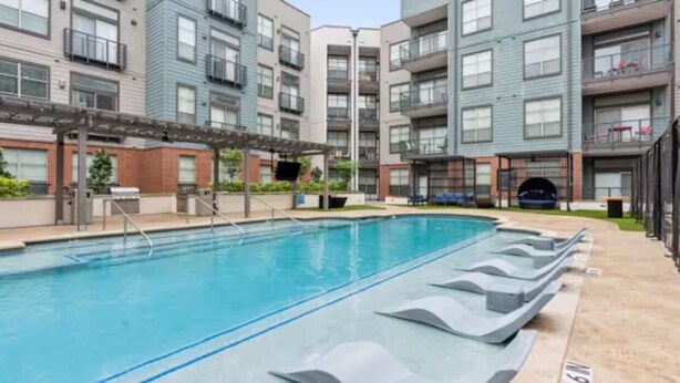 Una piscina con sillones de descanso, rodeada de edificios residenciales de varios pisos con balcones.