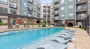 Une piscine entourée de chaises longues, elle-même bordée d’immeubles résidentiels à plusieurs étages dotés de balcons.