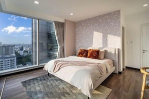 A bedroom with a large window, a bed with pillows, a radiator, and a wooden floor. - Salute de Sailing Tower - Palace Garden District 1 (Ho Chi Minh City)