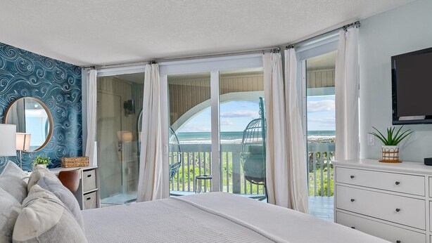 A bedroom with a large bed, a TV, a dresser, and a balcony with a view of the ocean. - Lovely ocean-view condo with pools, hot tubs, private W/D, & central AC (St. Augustine)